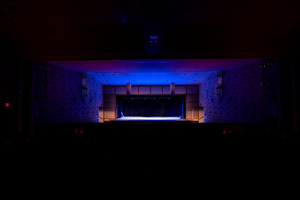 An Empty Dark Theatre With A Stage Illuminating Neon Blue.