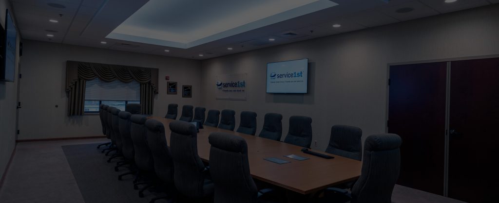 Inside Of A Conference Room With A Television And Gray Chairs Surrounding A Table.